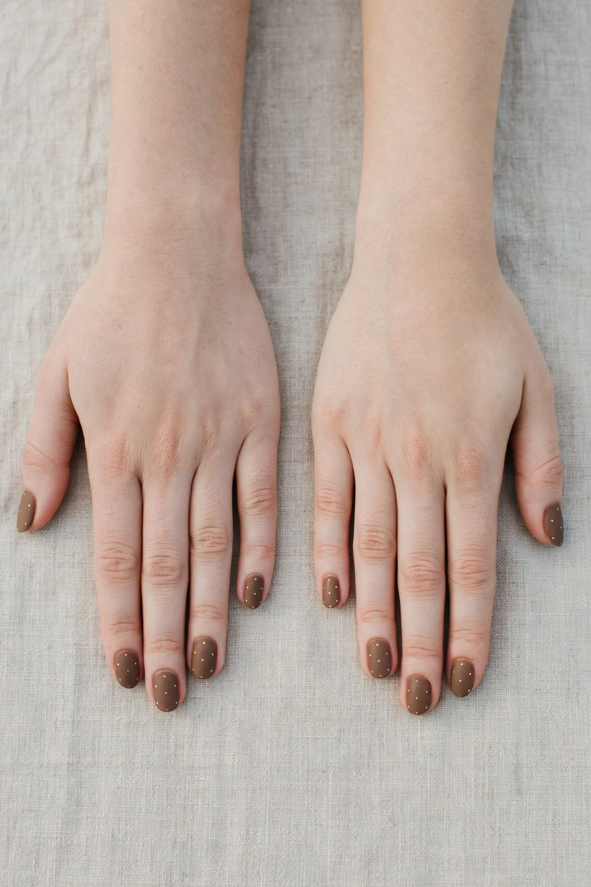 Oval Brown Neutral Matte Christmas Nails with a satin finish and tiny gold dots