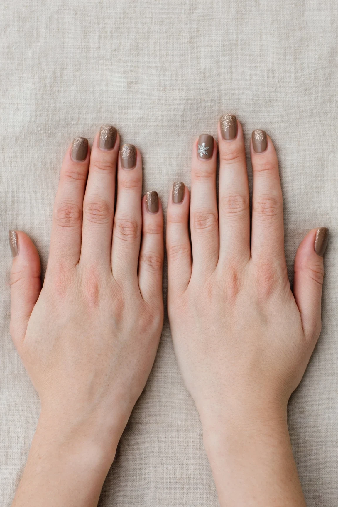 Short Oval Brown Neutral Matte Christmas Nails with a glitter gradient finish and a delicate snowflake on the ring finger