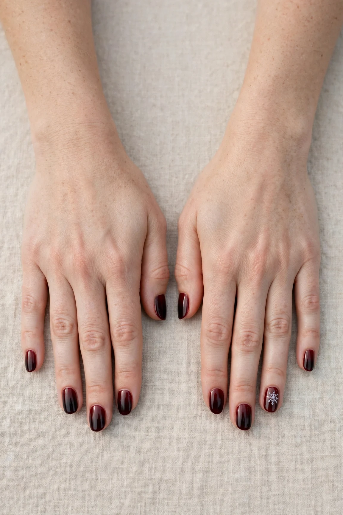 Short Oval Cherry Cola Ombre Nails with a high-gloss finish and a delicate snowflake on the ring finger