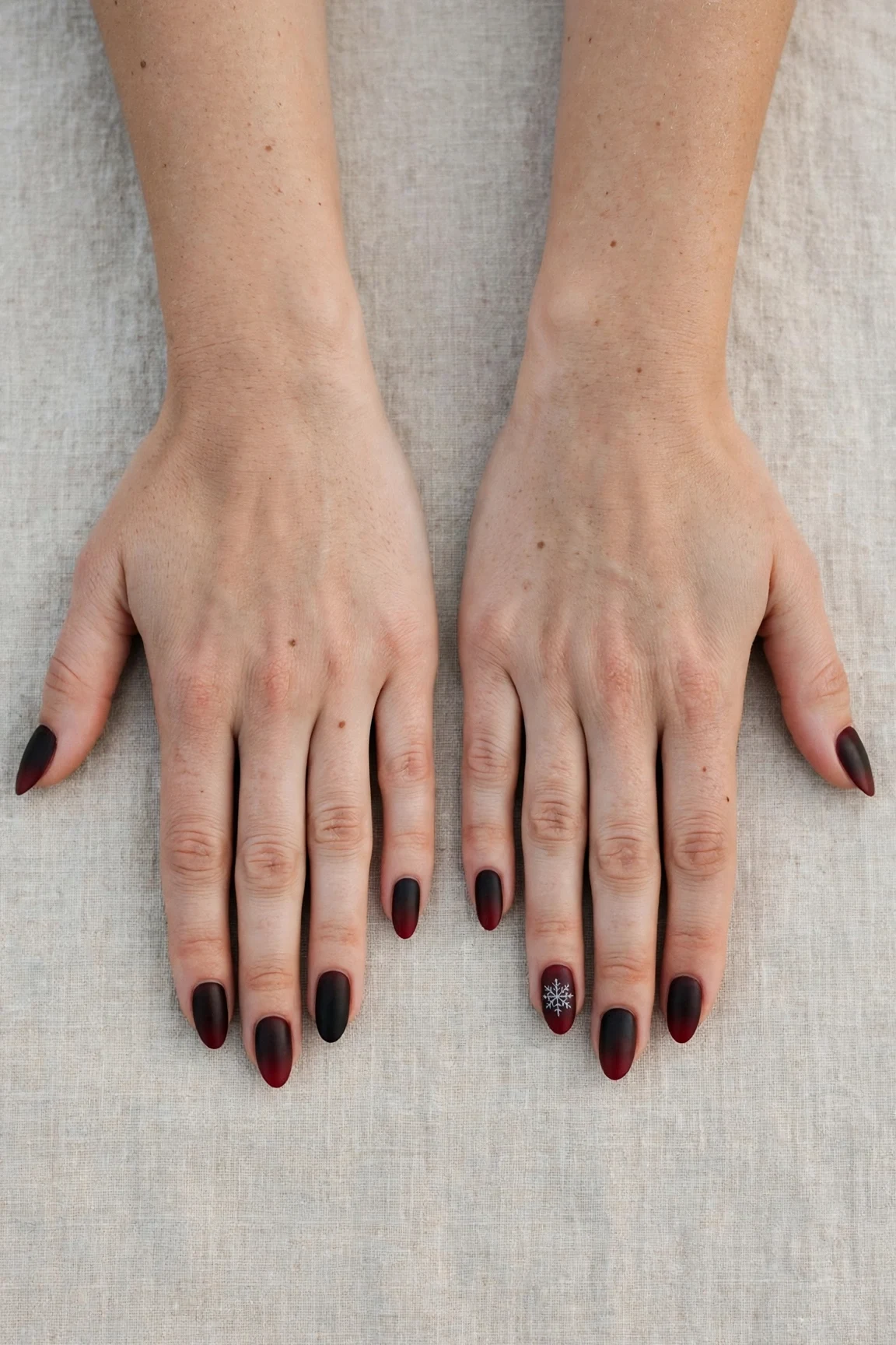 Almond Cherry Cola Ombre Nails with a soft matte finish and a delicate snowflake on the ring finger