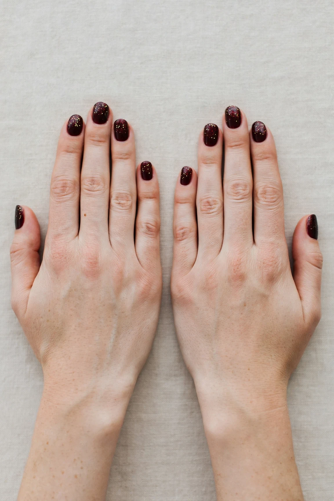 Short Oval Cherry Cola Velvet Finish Nails with a glitter gradient finish and tiny gold dots