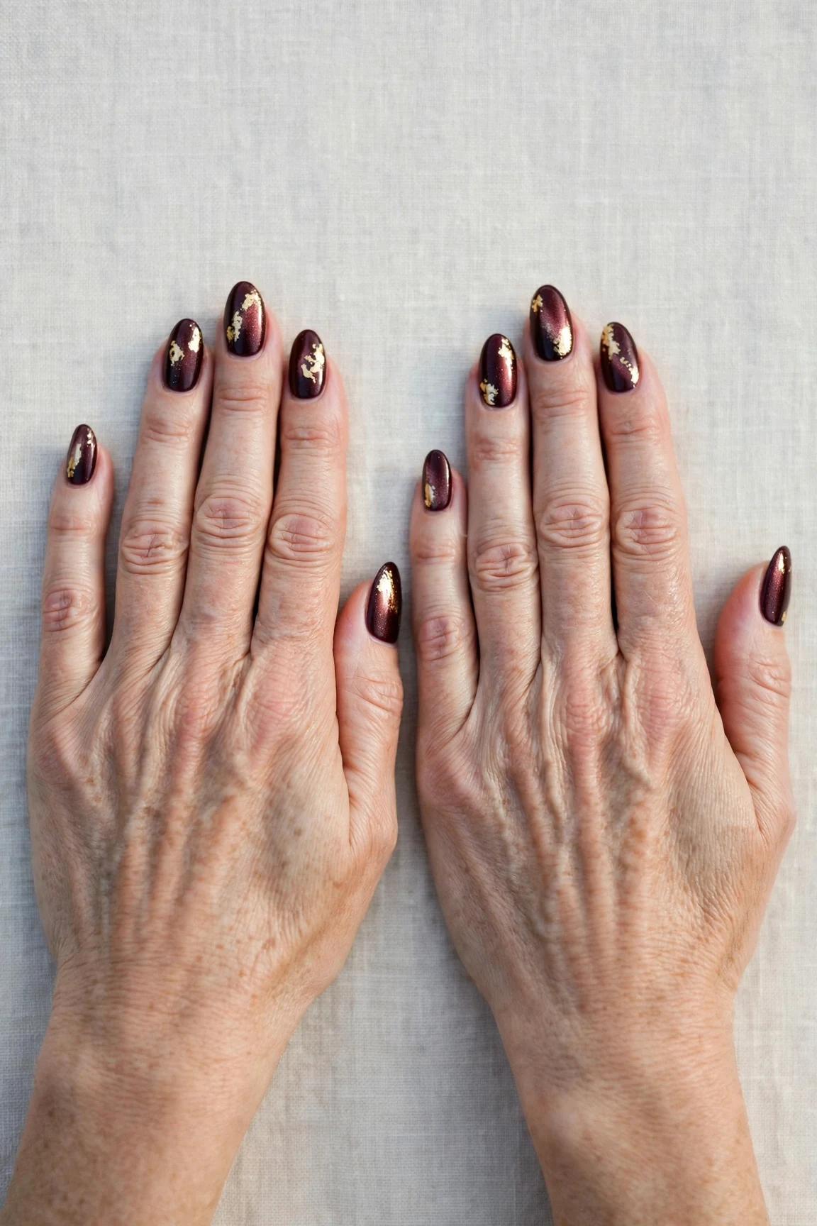Dark Cherry Velvet Almond Nails with a pearl shimmer finish and gold foil accents