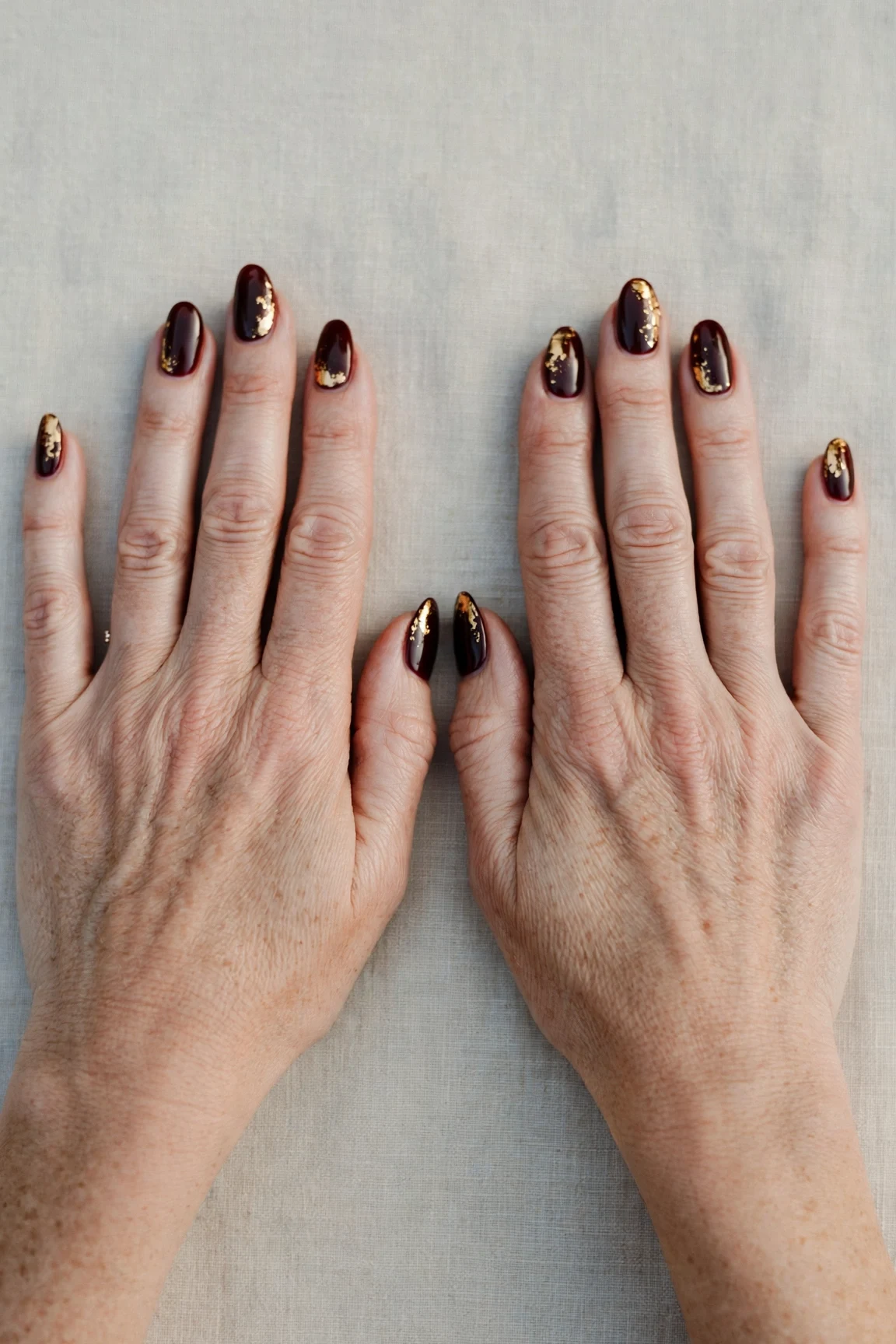 Dark Cherry Velvet Almond Nails with a deep glossy shine and gold foil accents