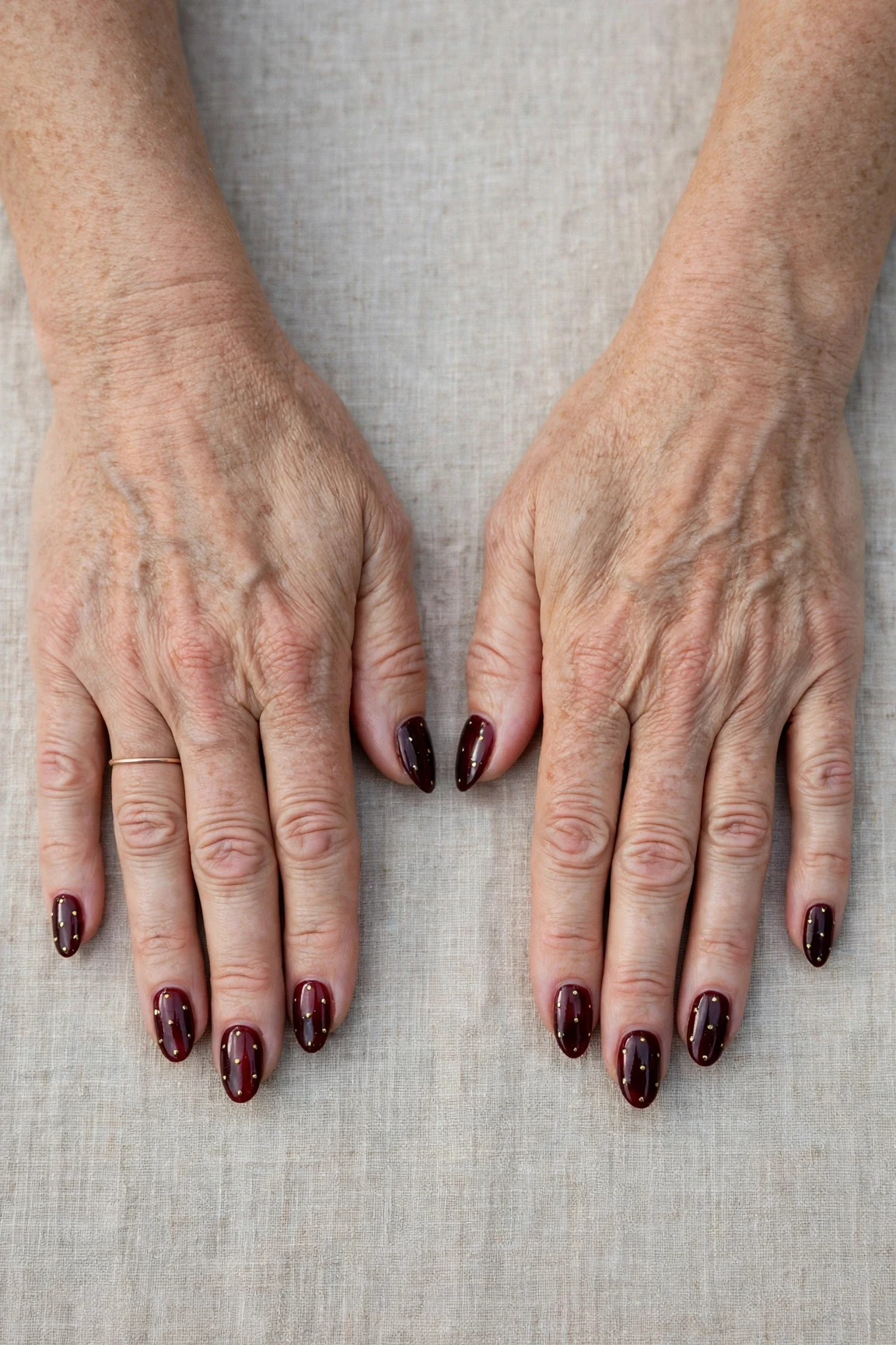 Dark Cherry Velvet Almond Nails with a sheer jelly finish and tiny gold dots