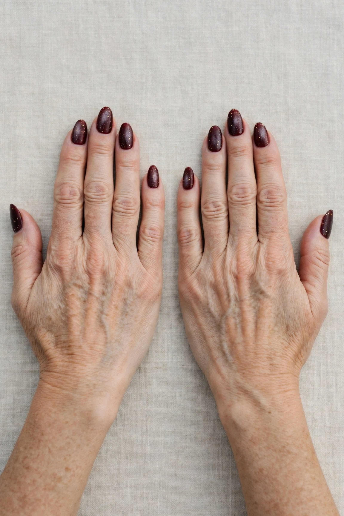 Dark Cherry Velvet Almond Nails with a frosted shimmer finish and tiny gold dots