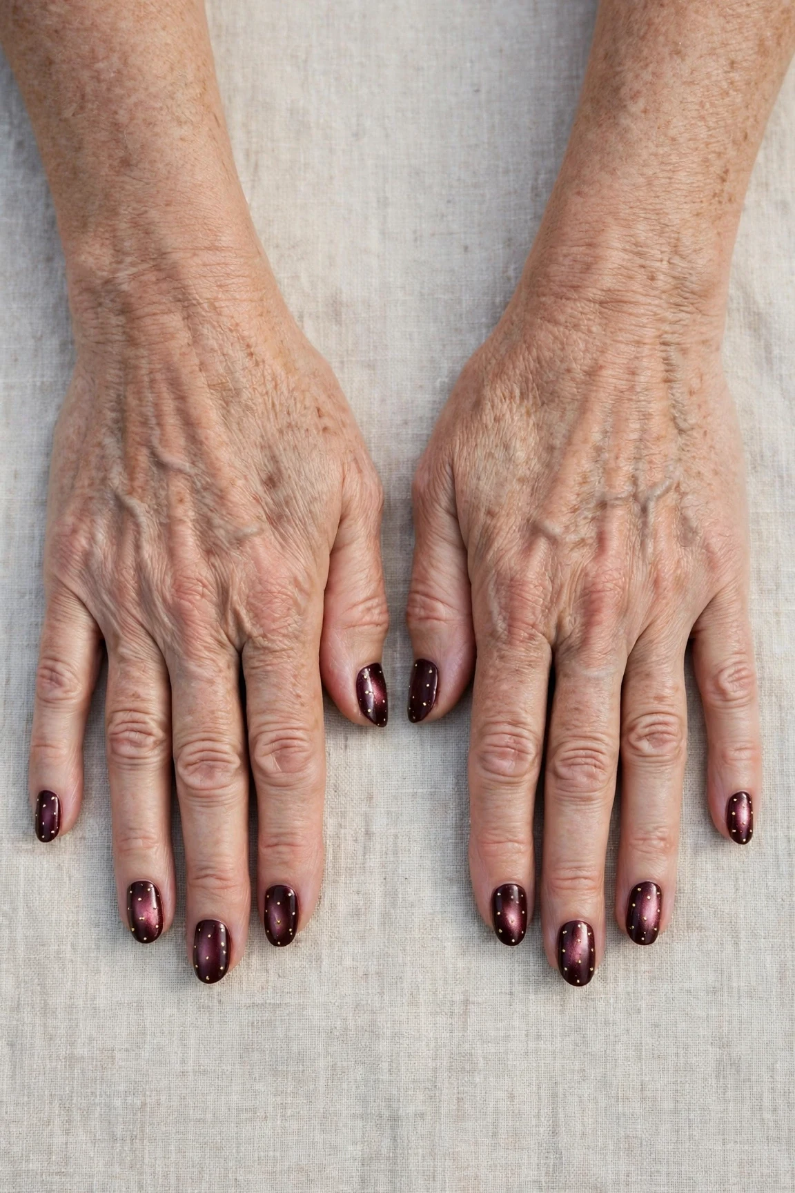 Dark Cherry Velvet Almond Nails with a pearl shimmer finish and tiny gold dots