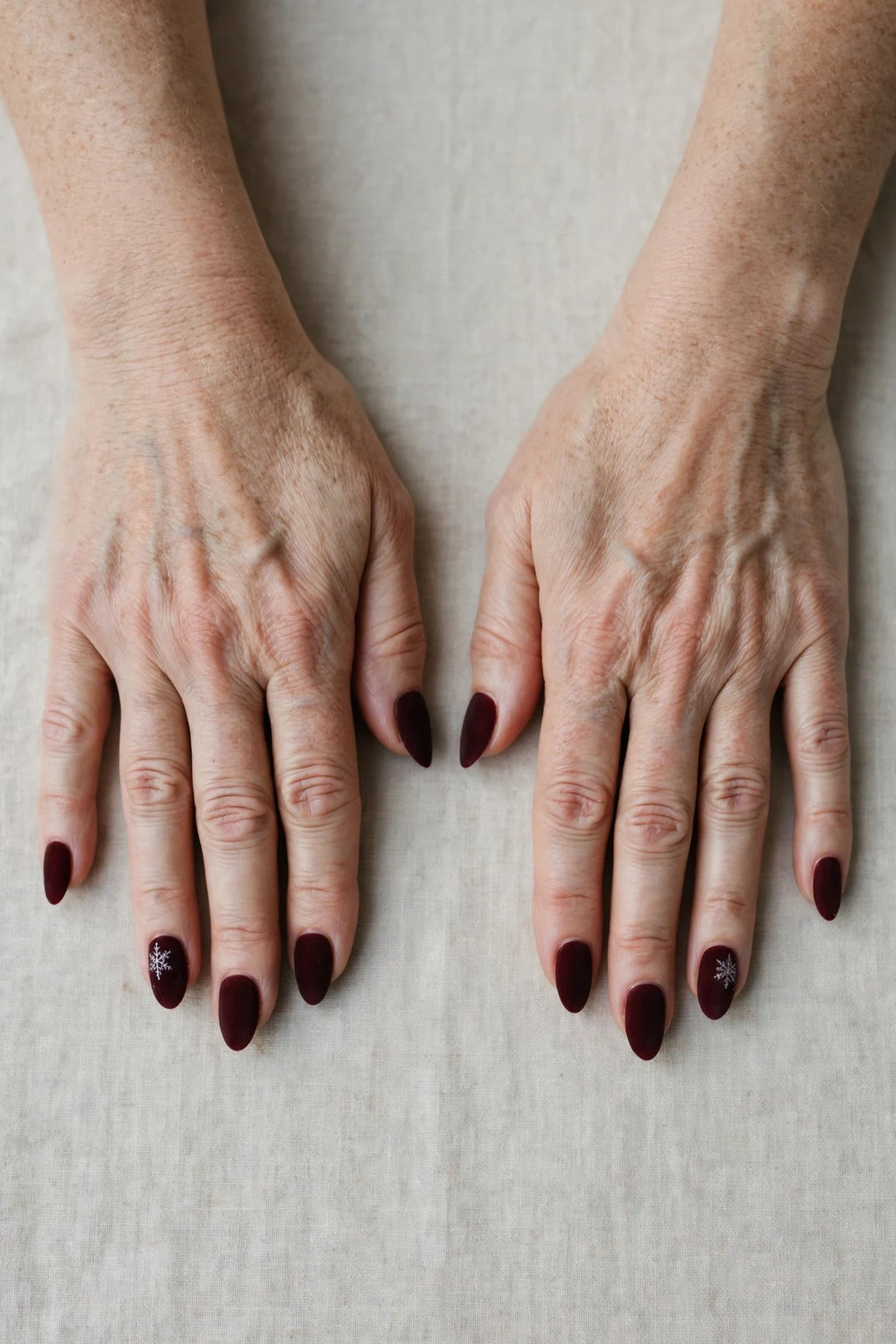 Almond Dark Cherry Velvet Manicure Ideas with a soft matte finish and a delicate snowflake on the ring finger