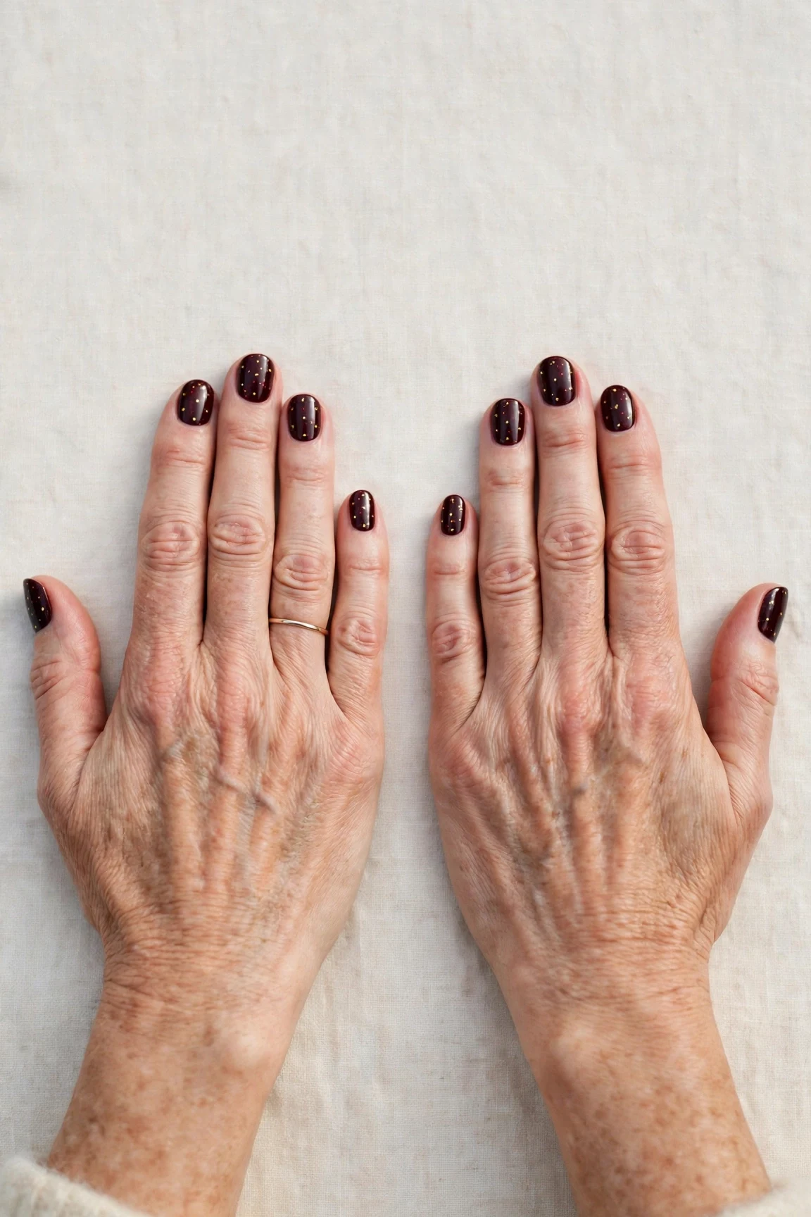 Short Oval Dark Cherry Velvet Nails with a high-gloss finish and tiny gold dots