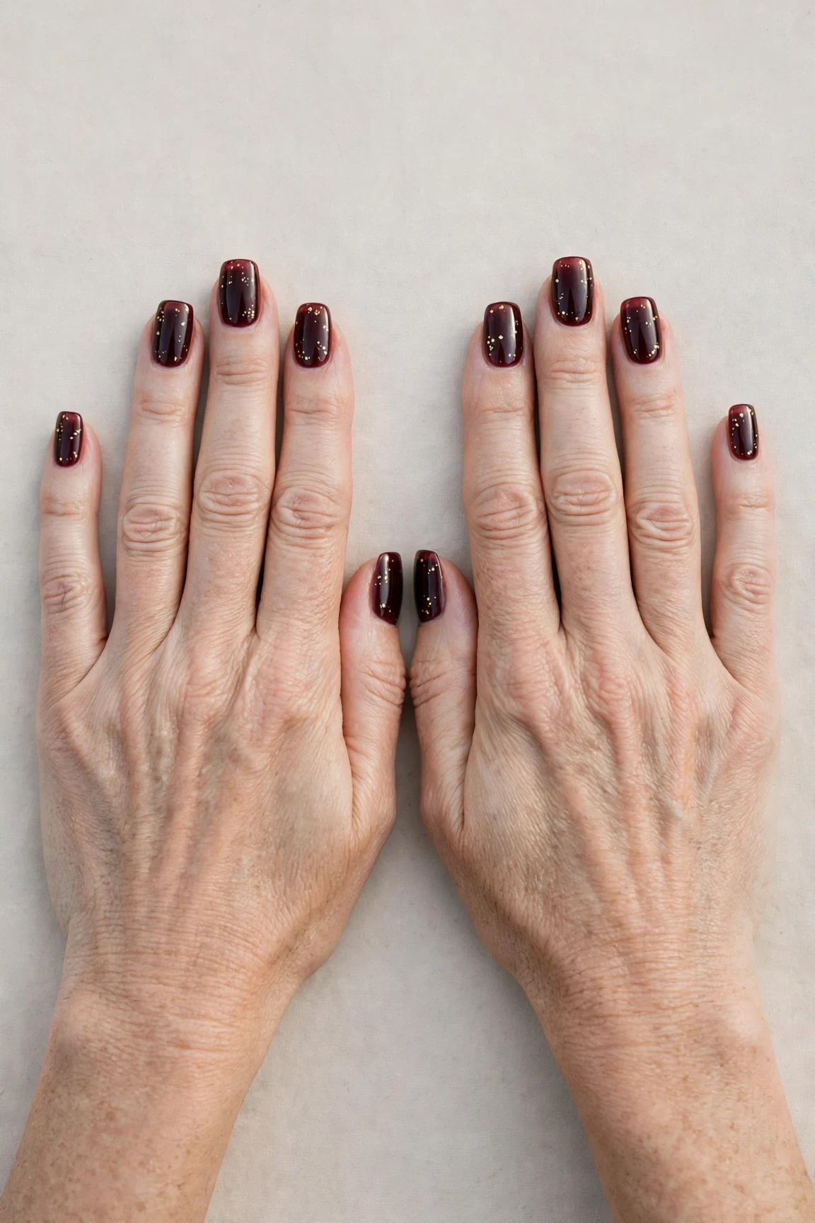 Squoval Dark Cherry Velvet Nails with a sheer jelly finish and tiny gold dots