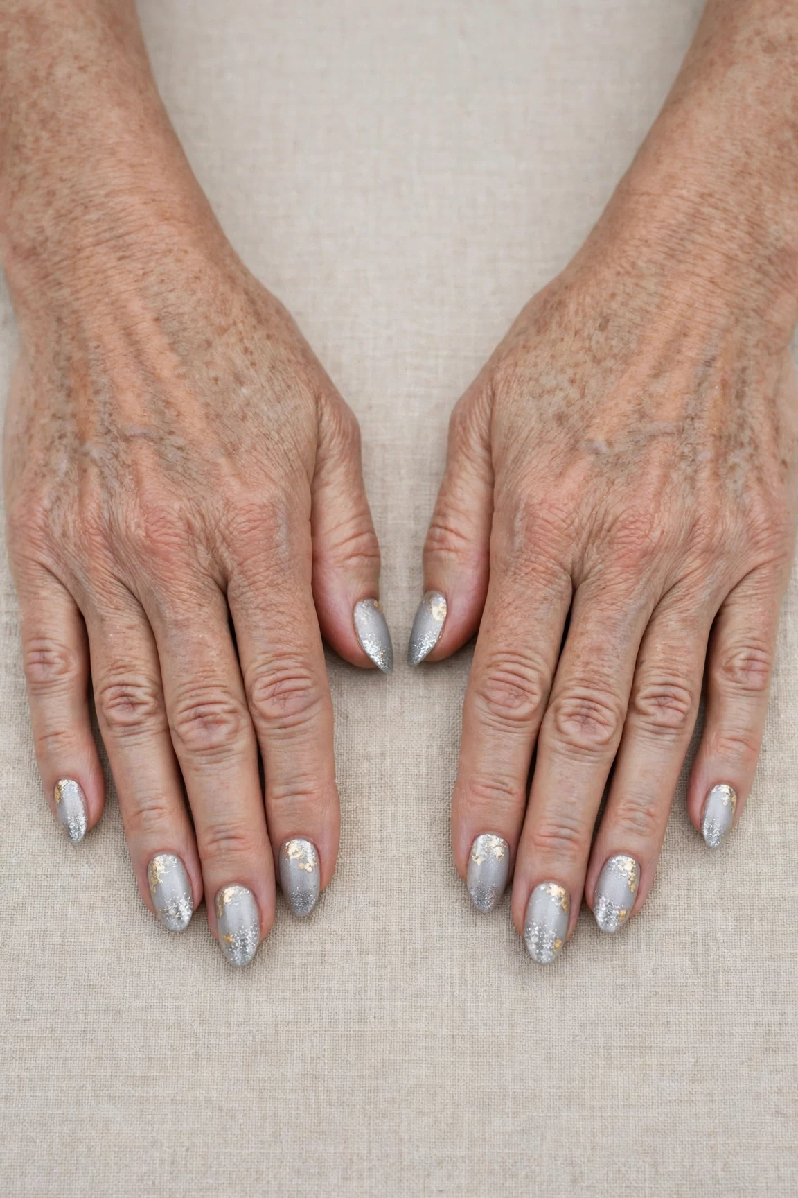 Icy Silver Frosted Almond Nails with a glitter gradient finish and gold foil accents