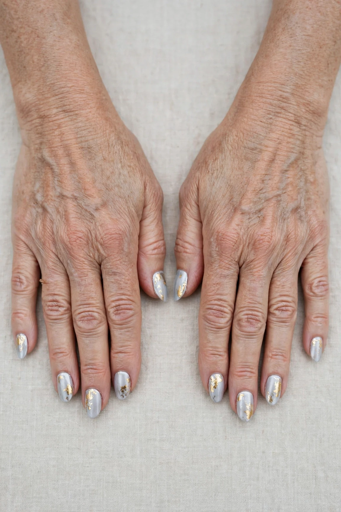 Icy Silver Frosted Almond Nails with a creamy opaque finish and gold foil accents