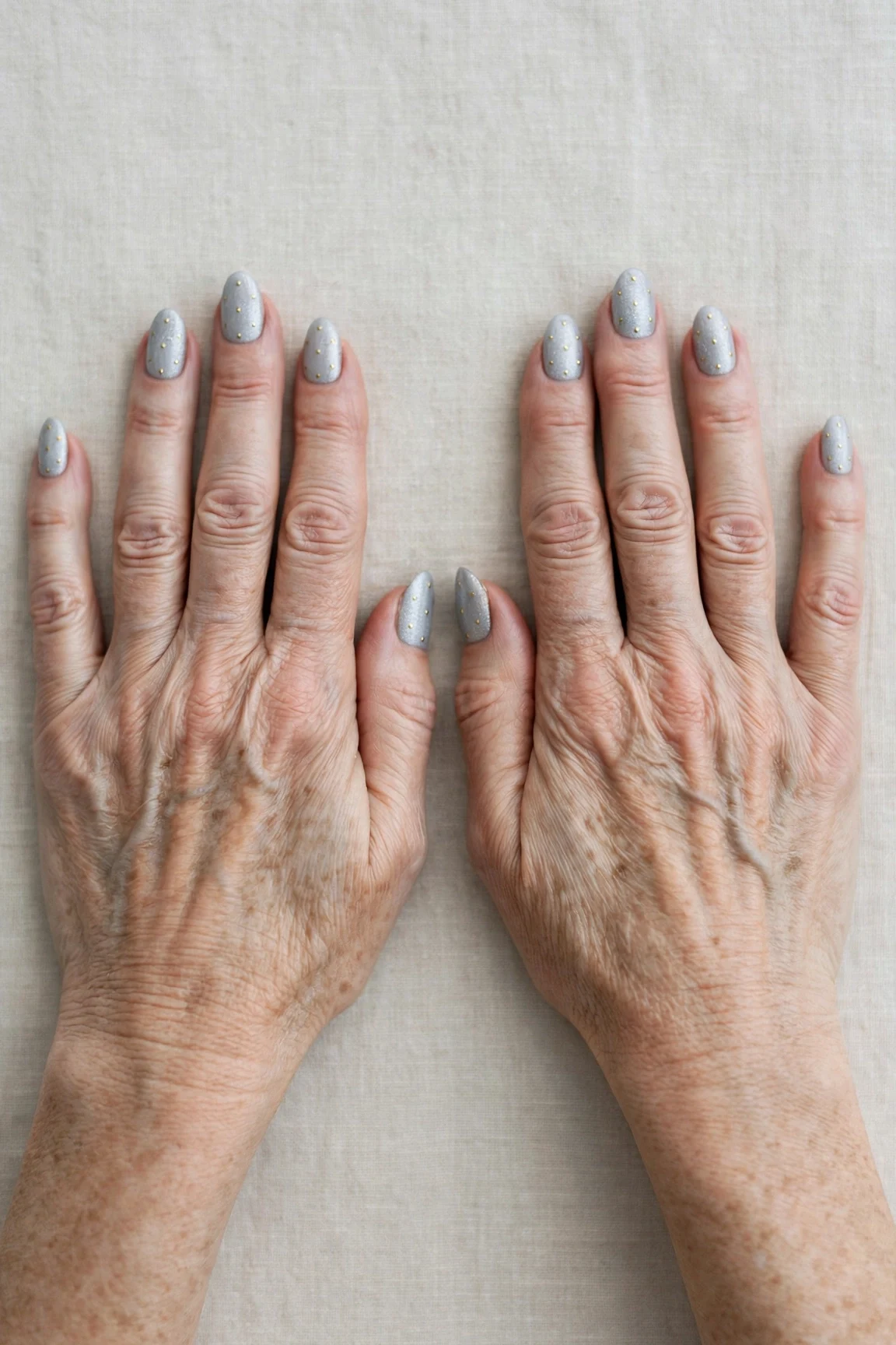 Icy Silver Frosted Almond Nails with a soft matte finish and tiny gold dots