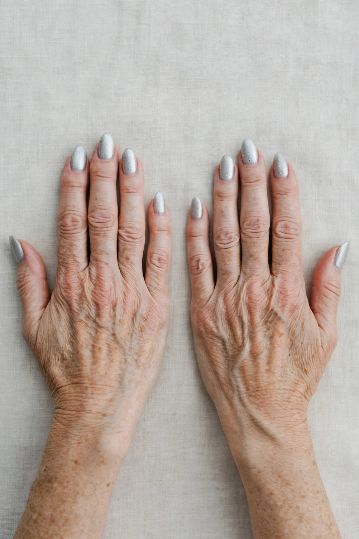 Icy Silver Frosted Almond Nails with a sheer jelly finish and tiny gold dots