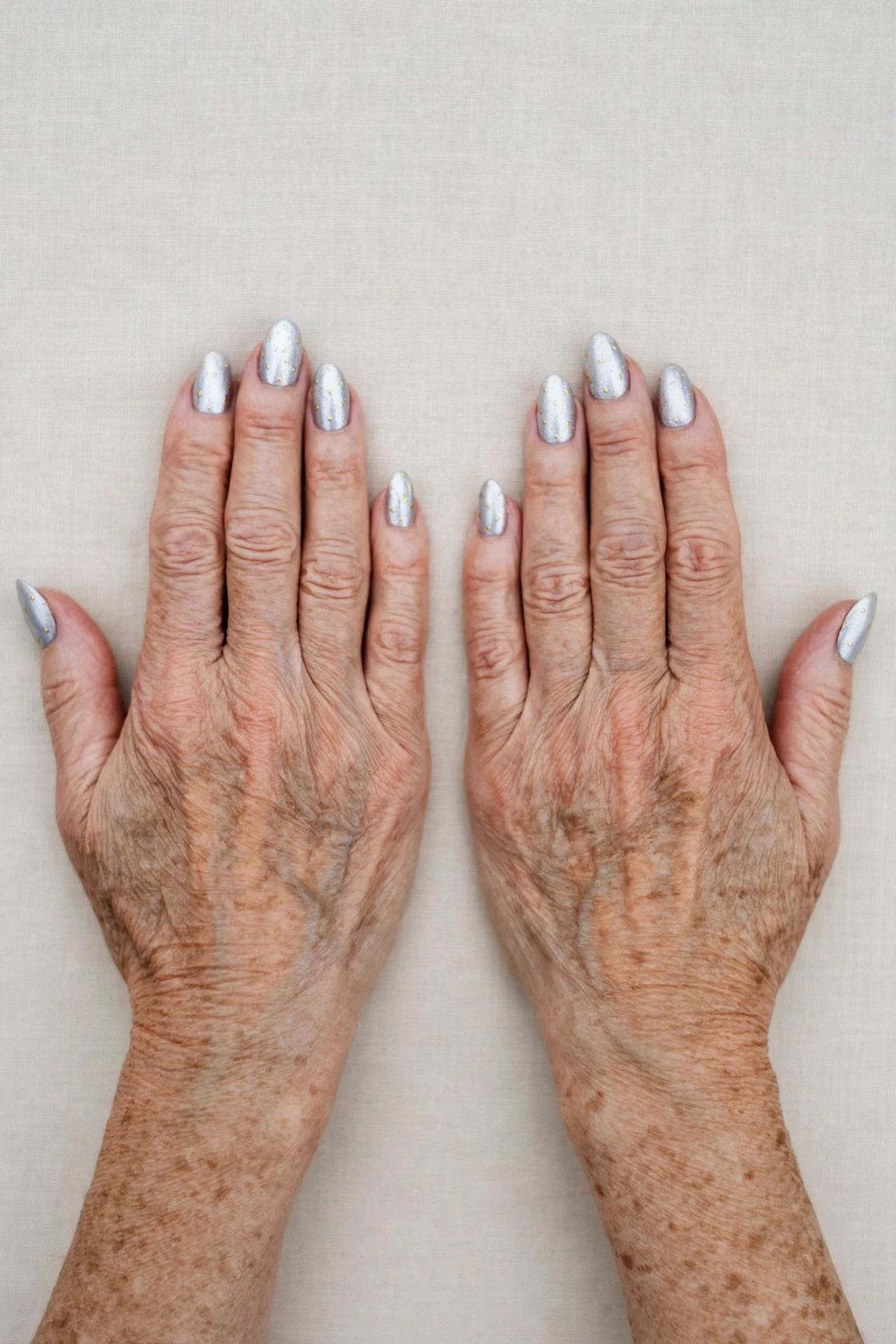 Icy Silver Frosted Almond Nails with a pearl shimmer finish and tiny gold dots