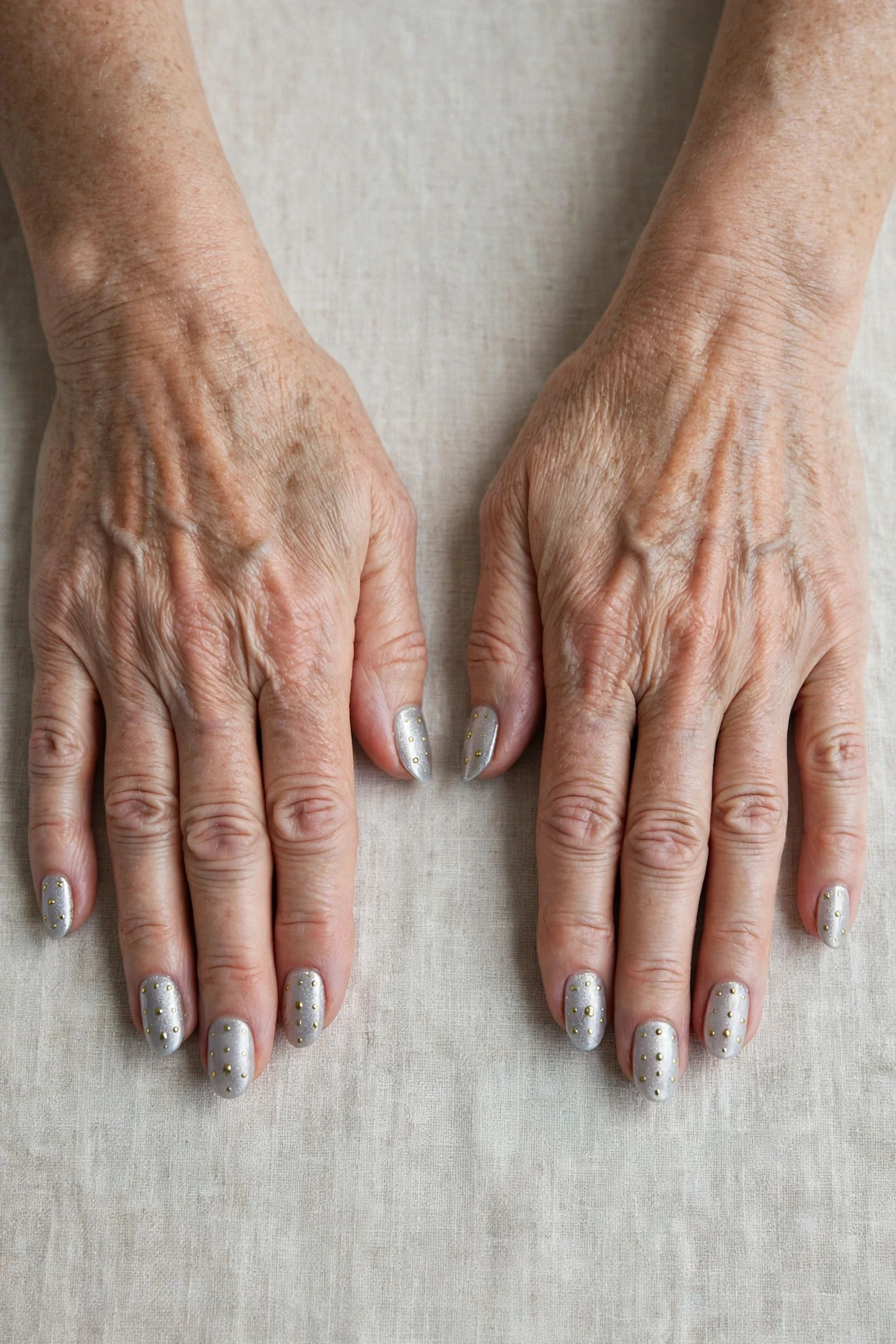 Icy Silver Frosted Almond Nails with a glassy gel finish and tiny gold dots