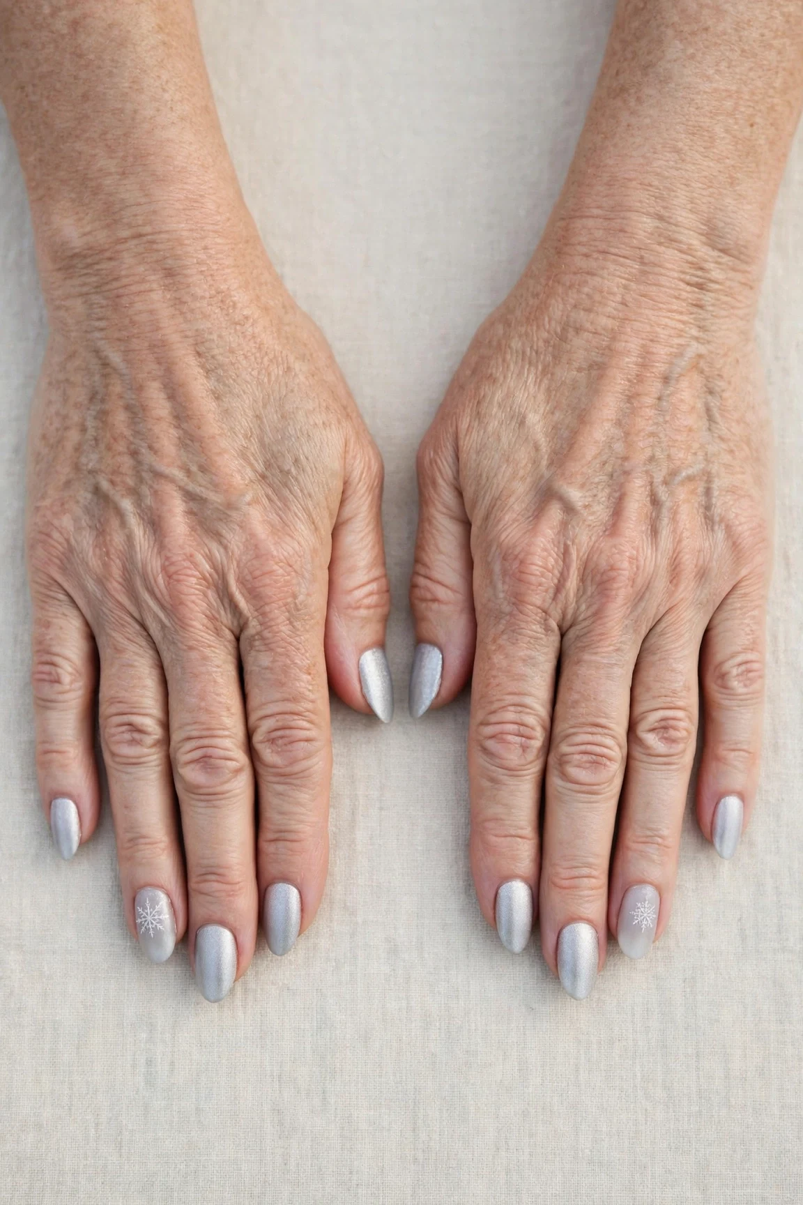 Icy Silver Frosted Almond Nails with a velvet matte finish and a delicate snowflake on the ring finger